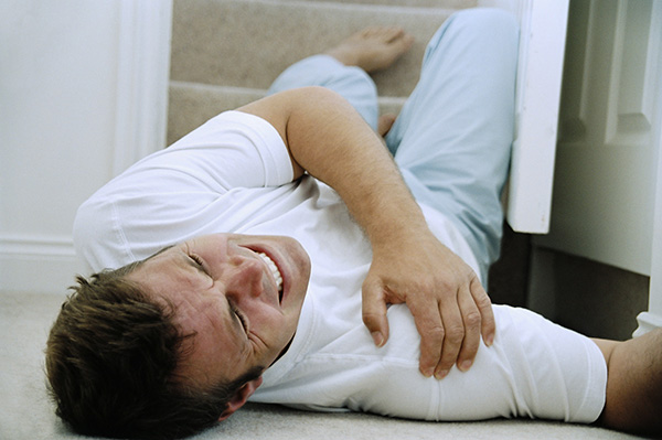 man holding shoulder at the bottom of the stairs after falling